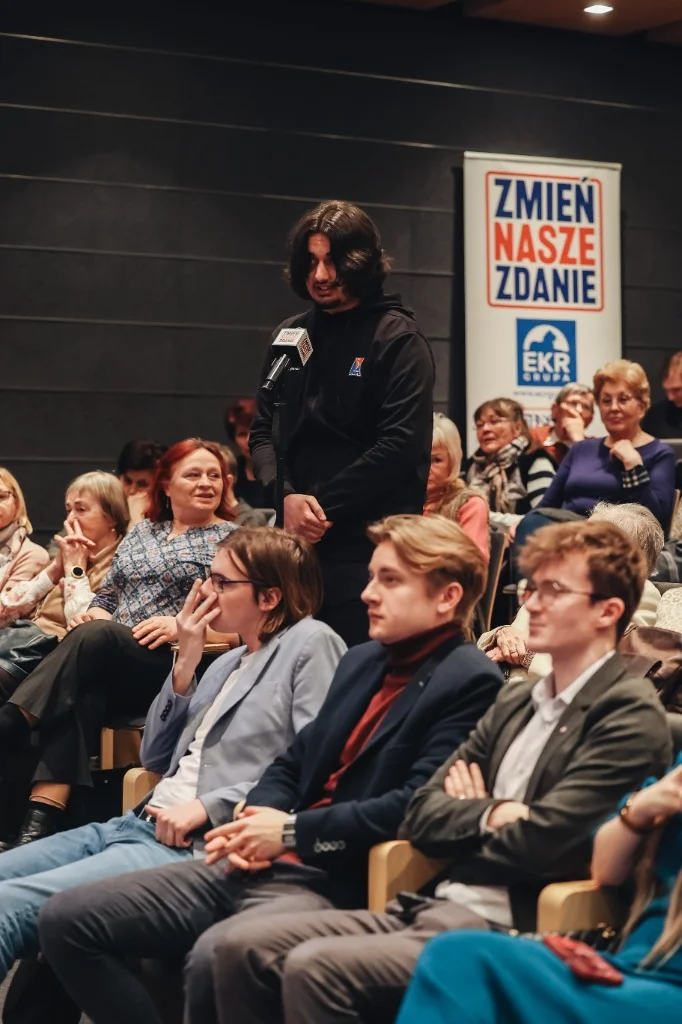 Uczestnik zadający pytanie z mikrofonem podczas spotkania Zmień Nasze Zdanie.