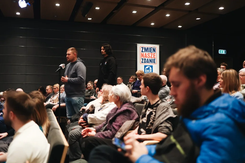 Młody uczestnik zadający pytanie do mikrofonu na sali podczas spotkania Zmień Nasze Zdanie.
